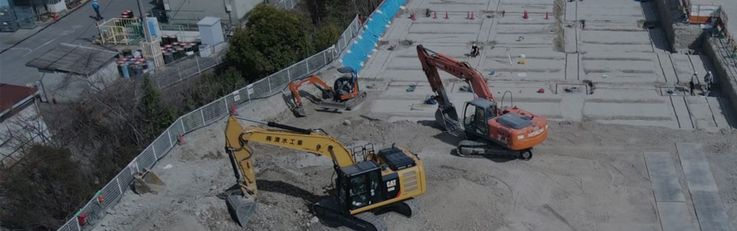 工事現場にオレンジの重機2台と黄色の重機が1台ある