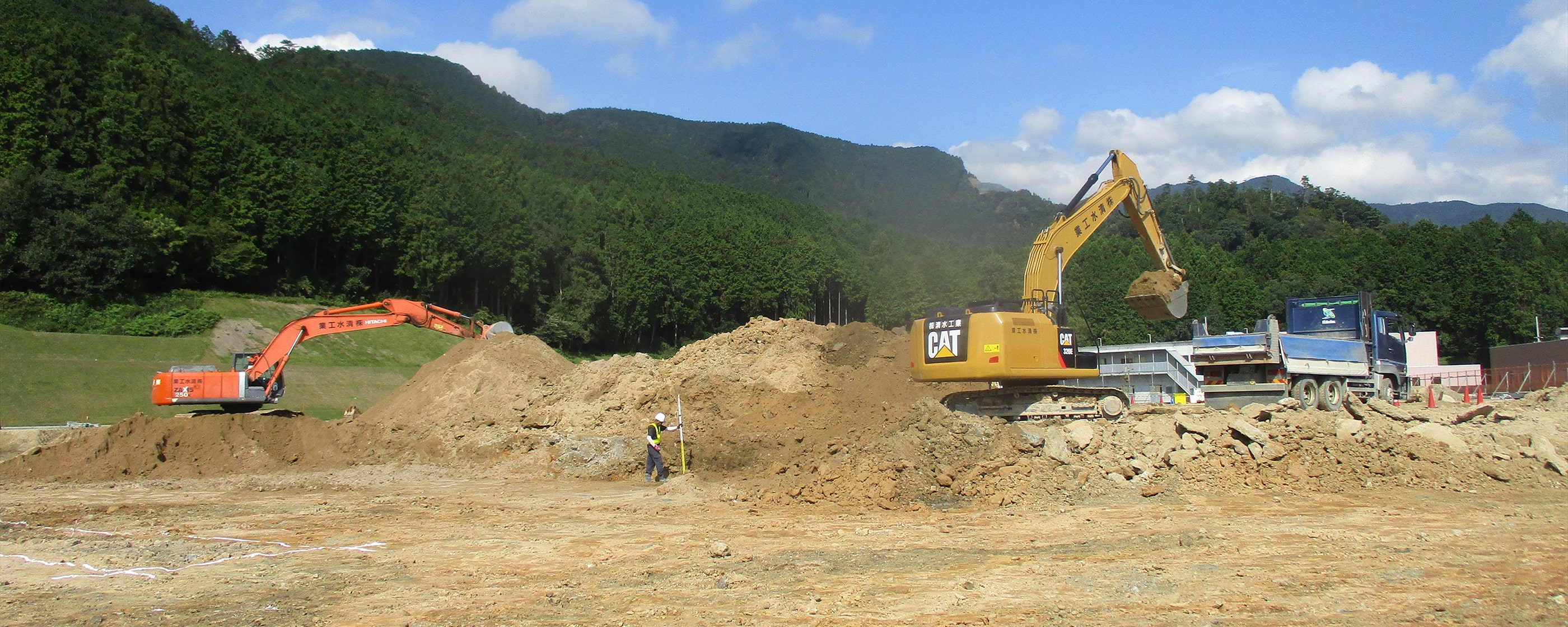 山間部の建設現場で重機が土を掘削している様子