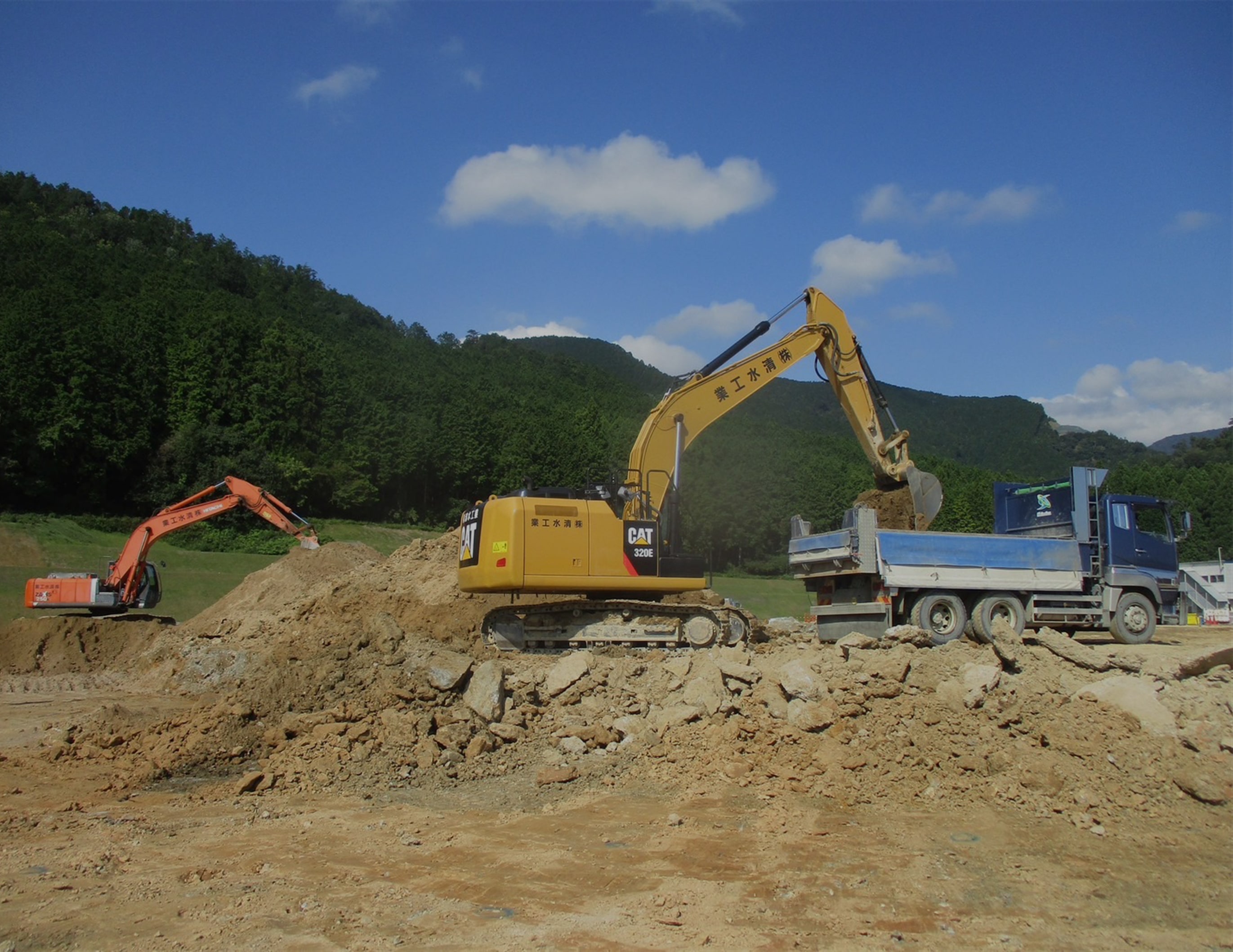 トラックの荷台にショベルカーを使って土を運んでいる
